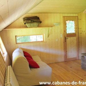 Cabane en bois à Bourgogne-Franche-Comté, intérieur chaleureux avec canapé et fenêtres lumineuses.
