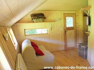 Cabane en bois à Bourgogne-Franche-Comté, intérieur chaleureux avec canapé et fenêtres lumineuses.