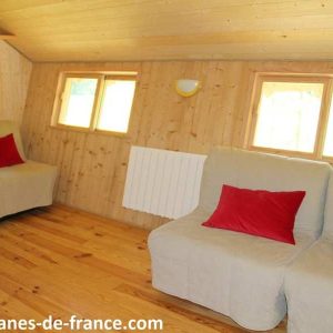 Cottage en bois chaleureux avec canapés confortables et grandes fenêtres lumineuses.