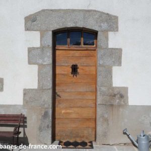 Porte en bois dune cabane insolite à Limousin, entourée de pierres et fleurs.