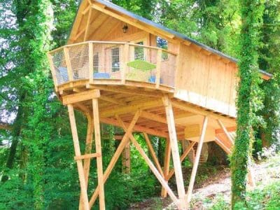 Cabane perchée en bois dans les arbres, entourée de verdure en Bourgogne-Franche-Comté.