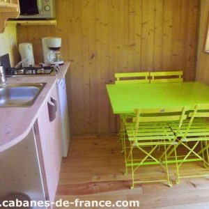 Cabane en bois à Bourgogne-Franche-Comté avec une table verte et cuisine équipée.