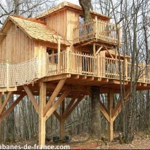 Cabane perchée en bois dans les arbres, avec balcons et vue sur la forêt.