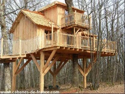 Cabane perchée en bois dans les arbres, avec balcons et vue sur la forêt.