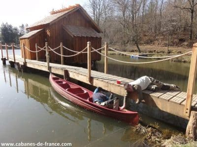 Cabane en bois sur pilotis au bord dun lac, avec un canoë rouge amarré.