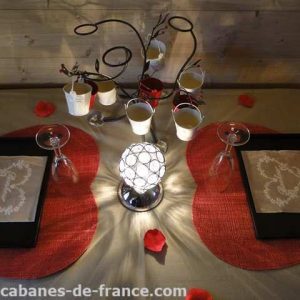 Table romantique dans une cabane en bois, décorée de pétales de rose et lanternes.