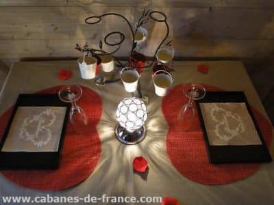 Table romantique dans une cabane en bois, décorée de pétales de rose et lanternes.