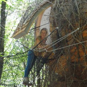Cabane dans les arbres en Aquitaine, entourée de verdure, avec un filet suspendu.