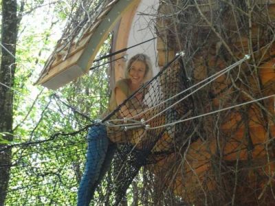 Cabane dans les arbres en Aquitaine, entourée de verdure, avec un filet suspendu.