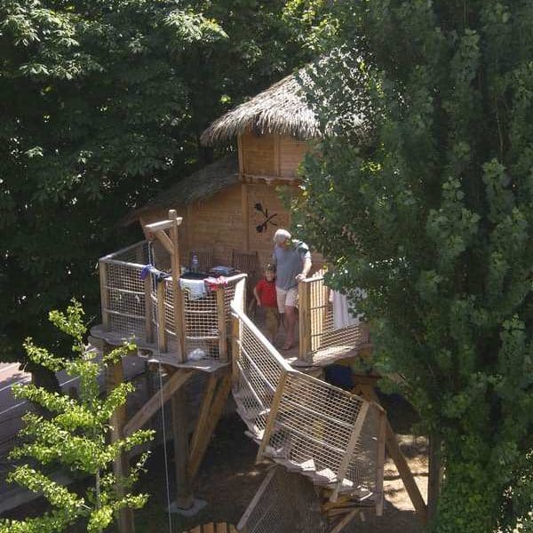 Cabane perchée dans les arbres, entourée de verdure, avec une terrasse en bois.