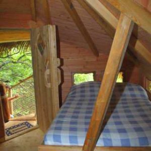 Cabane perchée en Auvergne, avec un lit à baldaquin et des murs en bois chaleureux.