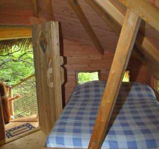 Cabane perchée en Auvergne, avec un lit à baldaquin et des murs en bois chaleureux.