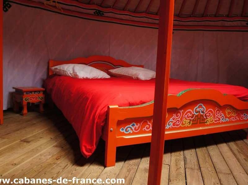 Chambre colorée dans une yourte en Auvergne, lit douillet et décor traditionnel.