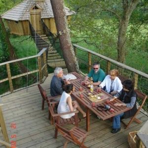 Cabane dans les arbres en Bretagne, avec une terrasse en bois et des convives autour dune table.