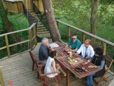 Cabane dans les arbres en Bretagne, avec une terrasse en bois et des convives autour dune table.