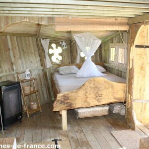 Cabane en bois en Bretagne, avec lit en bois sculpté et fenêtres décoratives.