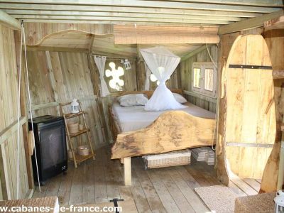 Cabane en bois en Bretagne, avec lit en bois sculpté et fenêtres décoratives.