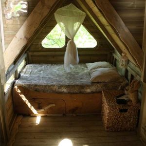 Cabane en bois en Bretagne, lit douillet sous un plafond en pente et lumière douce.