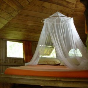 Cabane en bois en Bretagne avec un lit à baldaquin et une ambiance chaleureuse.