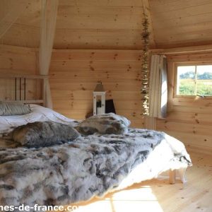 Cabane en bois en Bretagne, lit douillet avec couverture en fourrure et vue sur la nature.