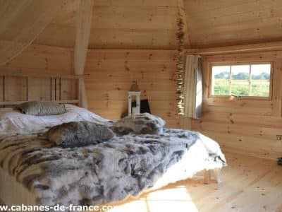 Cabane en bois en Bretagne, lit douillet avec couverture en fourrure et vue sur la nature.