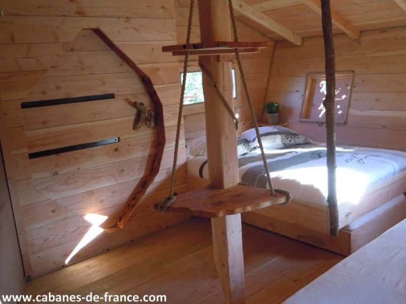Cabane en bois en Bretagne avec un lit douillet et une balançoire en bois.