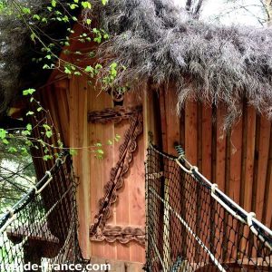 Cabane perchée en bois avec toit en chaume, entourée de verdure en Auvergne.