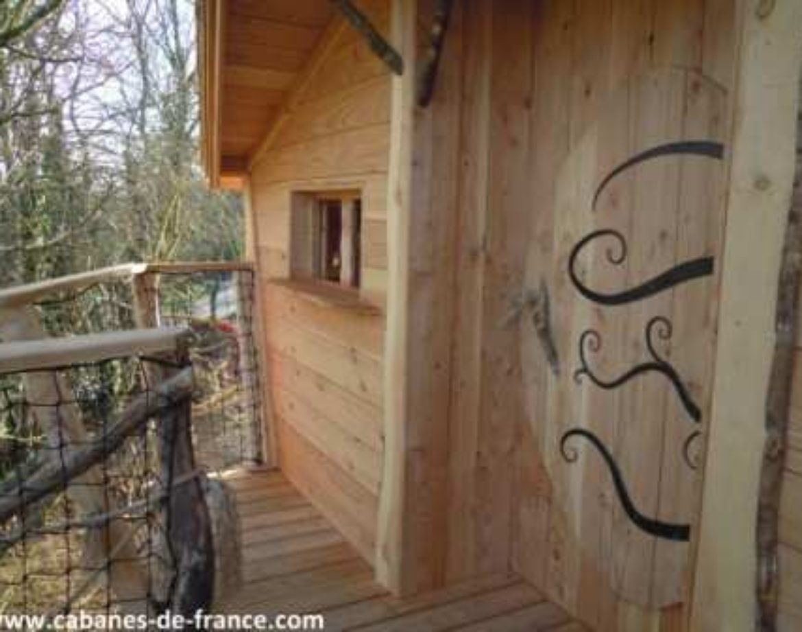 Cabane en bois perchée, avec un balcon en bois et une porte décorative originale.