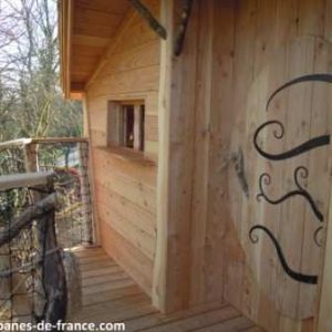 Cabane en bois perchée, avec un balcon en bois et une porte décorative originale.