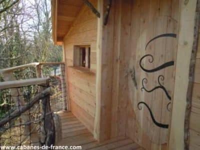 Cabane en bois perchée, avec un balcon en bois et une porte décorative originale.