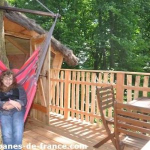 Cabane dans les arbres avec hamac coloré et vue sur la forêt verdoyante.