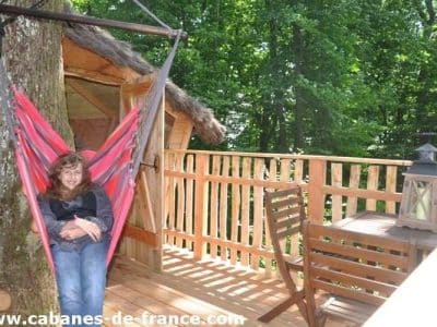 Cabane dans les arbres avec hamac coloré et vue sur la forêt verdoyante.
