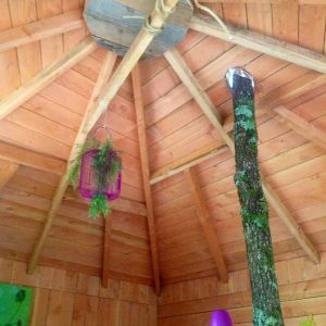 Cabane en bois avec un tronc darbre au centre et des lampes colorées.