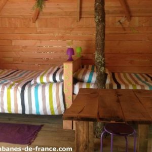 Cabane en bois colorée avec lits rayés et table en bois, au cœur de la nature.