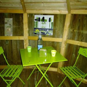 Cabane en bois à Champagne-Ardenne, avec table et chaises vertes vives.