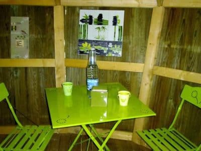 Cabane en bois à Champagne-Ardenne, avec table et chaises vertes vives.