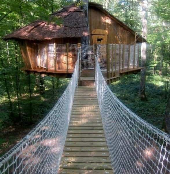 Cabane perchée dans les arbres, accessible par un pont suspendu en bois.