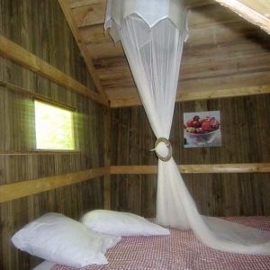 Cabane en bois à Champagne-Ardennes, lit douillet avec voilage élégant.