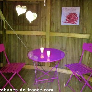Cabane en bois à Champagne-Ardennes avec table et chaises roses, ambiance romantique.