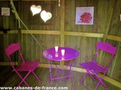 Cabane en bois à Champagne-Ardennes avec table et chaises roses, ambiance romantique.