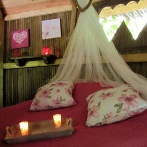 Cabane romantique en Champagne-Ardenne, lit douillet avec coussins fleuris et bougies.