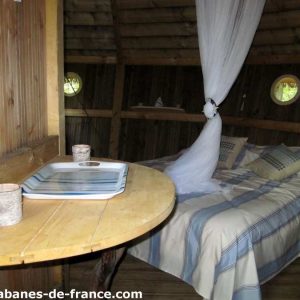 Cabane en bois à Champagne-Ardennes, avec un lit douillet et des fenêtres rondes.