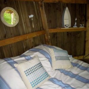 Cabane en bois à Champagne-Ardenne, lit douillet avec coussins à motifs.