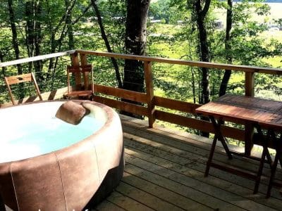 Cabane perchée en Midi-Pyrénées avec jacuzzi sur la terrasse boisée.