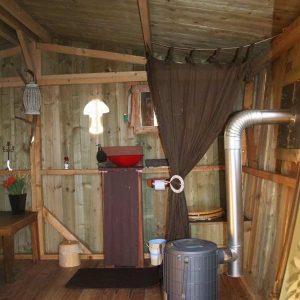 Cabane en bois à Basse-Normandie, intérieur chaleureux avec lavabo rouge et poêle.