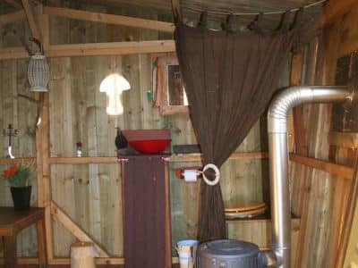 Cabane en bois à Basse-Normandie, intérieur chaleureux avec lavabo rouge et poêle.