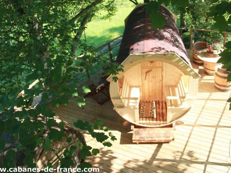 Hébergement insolite en Basse-Normandie : cabane en bois sur plateforme, entourée de verdure.