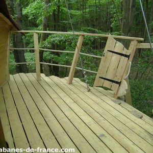 Cabane perchée en forêt, terrasse en bois offrant une vue sur la nature environnante.