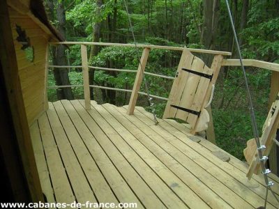 Cabane perchée en forêt, terrasse en bois offrant une vue sur la nature environnante.