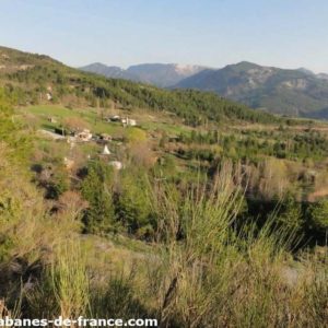 Cabanes en bois nichées dans la verdure, avec montagnes en arrière-plan.